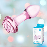 A pink glass anal toy with a rose-shaped base is showcased against a background featuring a soft, blurred gradient of pastel colors. A product box beside it displays the brand "Gläs" and describes it as the "5” Rosebud Glass Butt Plug," ideal for experimenting with temperature play.